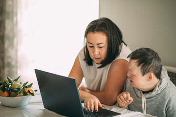 elderly woman with Down syndrome Sitting With Home Tutor Using Laptop For Lesson At Home