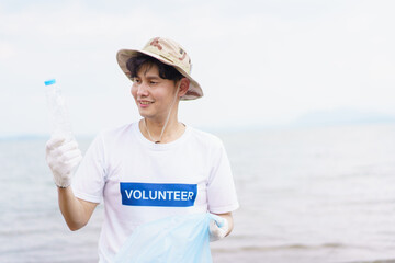 Asian young man picking up a plastic bottle garbage on the beach.