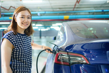 Beautiful Asian woman connecting a AC Type 2 EV charging connector to a vehicle, woman preparing an EV - electric vehicle charging connector for recharge a vehicle.