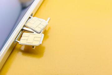 Broadband 5G mobile communication technology concept : SIM card tray / dual SIM card slot with two nano SIM cards on yellow background. SIM stores international mobile subscriber identity IMSI number. - obrazy, fototapety, plakaty