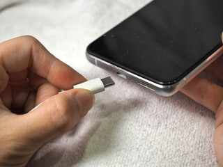 A person charges a mobile phone on a white background. Close up plugging in a USB Type-C (USB-C)...