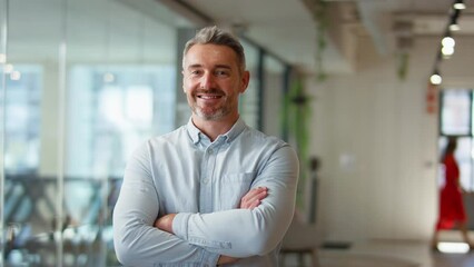 Camera tracks across smiling mature businessman standing in modern open plan office looking into camera - shot in slow motion - Powered by Adobe