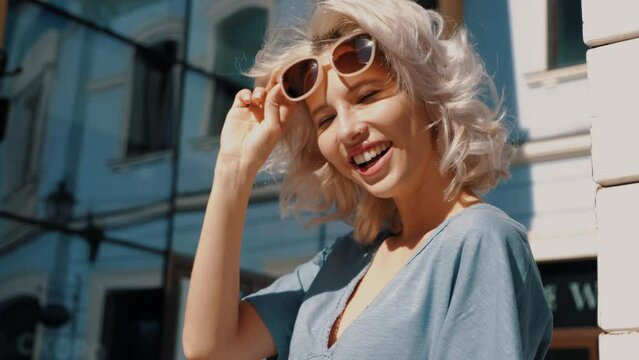 Young beautiful smiling hipster woman in trendy summer dress clothes. Sexy carefree model posing in the street at sunny day. Positive blond female outdoors. Cheerful and happy. In sunglasses