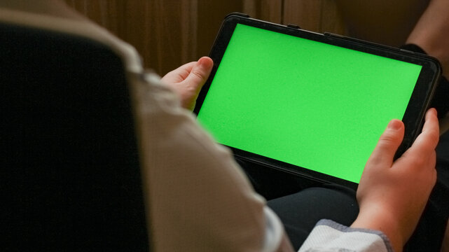 A Young Man Holds A Tablet With A Green Screen. Close-up. Home Furnishings. Chroma Key. View Over Shoulder.