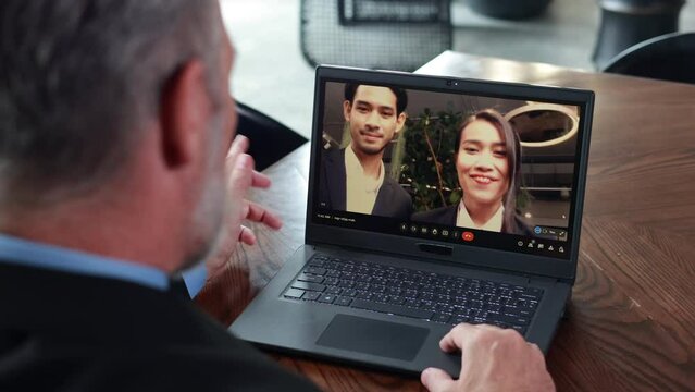 Back view of senior business man talking with business partners Asian male and female on Zoom video call programs at home office