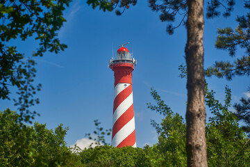 Lighthouse red white. Tower as a shipping signal between various green trees. Sunny summer day with...