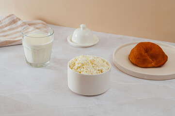 cottage cheese in a bowl, a bun on a plate. milk in a glass