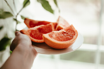 Person's hand holding a white plate of red healthy grapefruit slices