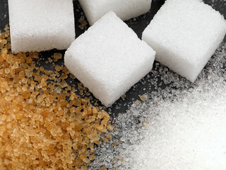 close up of three different types of sugar, white refined granulated sugar, brown cane sugar and sugar cubes