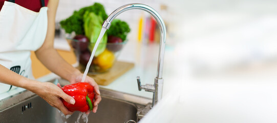 Happy healthy Asian woman washing a vegetables in domestic kitchen faucet before cooking. A...