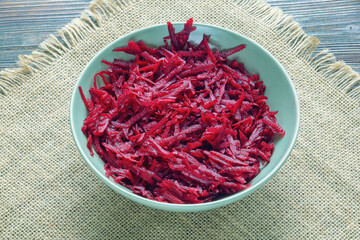 Grated red beetroot in bowl on dark rustic table