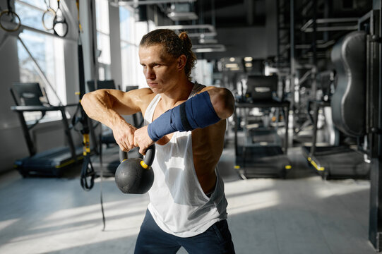 Handsome muscular man doing cross fit training with kettle bell lifting at gym