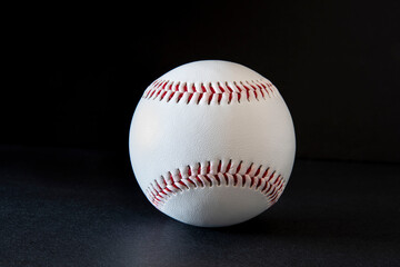 Close-up of a white baseball with red stitching on a black background