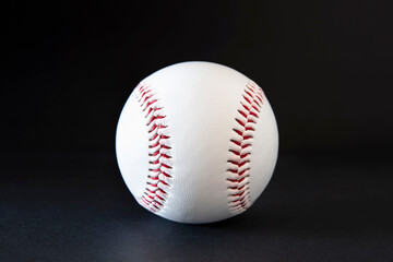 Close-up of a white baseball with red stitching on a black background