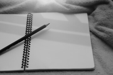 Monochrome image of notebook and pencil against sunlight and beautiful shadows with space for text. Selective focus.