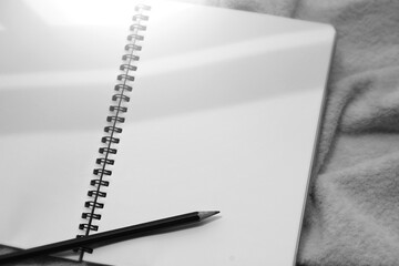 Monochrome image of notebook and pencil against sunlight and beautiful shadows with space for text. Selective focus.