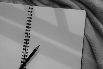 Monochrome image of notebook and pencil against sunlight and beautiful shadows with space for text. Selective focus.