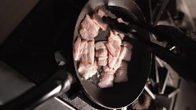 Caesar salad preparation process. Close-up of chef's hands turning over pieces of bacon in a frying pan