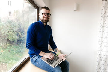 man in blue sweater and jeans is working alone at home with laptop