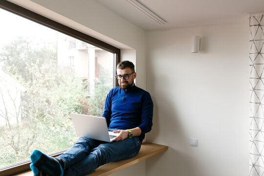 man in blue sweater and jeans is working alone at home with laptop