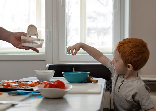 Child cooks with dad. The kid pours salt into a plate.