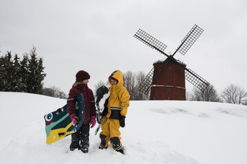 kids sledging in the snow next to a windmill