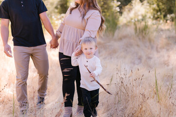 Adorable toddler carrying stick pulling mom and dad