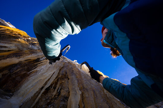 A woman with long hair ice climbing on a clear day