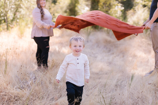 Adorable toddler running under blanket mom & dad holding