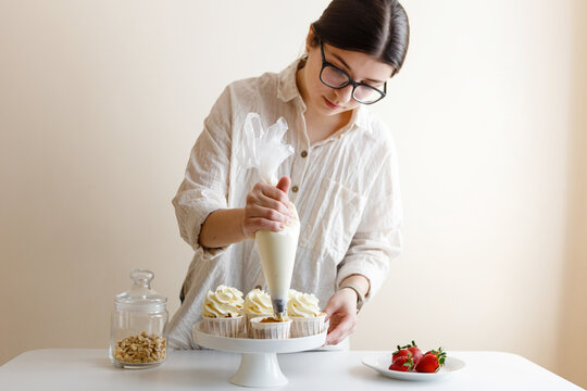 pastry chef girl prepares cupcakes with cream in the kitchen