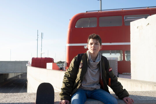 young man sitting on a fence with a skateboard leaning on wall
