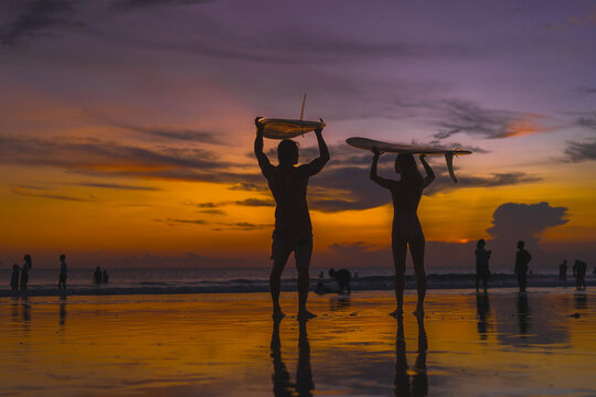 Surfers with surfboards at sunset, Bali.