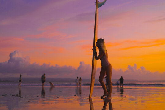 Woman surfer with surfboard at sunset, Bali.