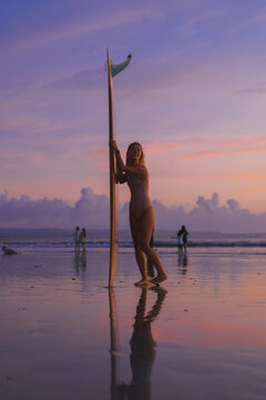 Woman surfer with surfboard at sunset, Bali.