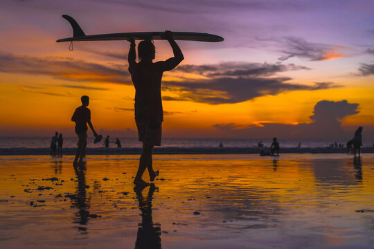Man surfer with surfboard at sunset, Bali.