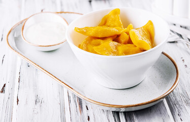 Yellow dumplings with sour cream on a plate closeup