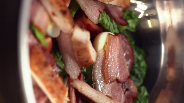 chef cooking caesar salad on restaurant kitchen, puts slices of fried bacon in a bowl