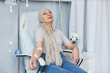 Portrait of tired senior woman sitting in chair with IV drip during chemotherapy treatment