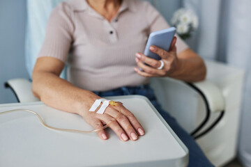 Close up of unrecognizable woman holding smartphone during IV drip treatment, copy space