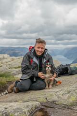 Caucasian hiker posing with a King Charles spaniel dog on the way to pulpit rock, Lysefjord, Norway, one of Norway most famous attractions.