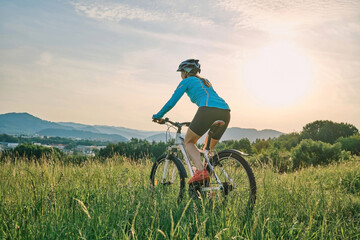 Fototapeta na wymiar Cyclist Woman riding bike in helmets go in sports outdoors on sunny day a mountain in the forest. Silhouette female at sunset. Fresh air. Health care, authenticity, sense of balance and calmness. 