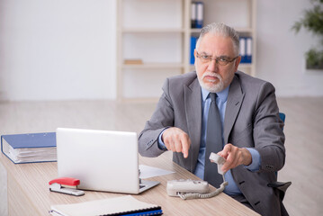Old male employee speaking by phone at workplace