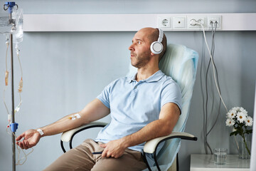 Side view portrait of adult man wearing headphones and listening to music during IV drip treatment...