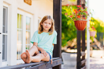 Cute sleepy girl sitting on the railing of the terrace of the house.