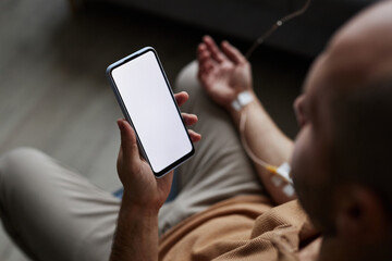 Closeup of adult man using smartphone with white screen mockup during IV drip treatment