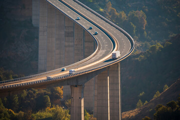 Huge viaduct crossing a ravine with a truck with a refrigerated semi-trailer and several other...