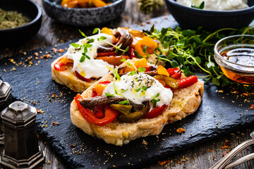 Tasty sandwiches - toasted bread with burrata cheese, anchovies, bell pepper, olives, tomatoes and...