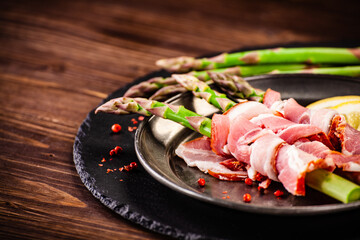 Uncooked green asparagus wrapped with bacon on wooden table