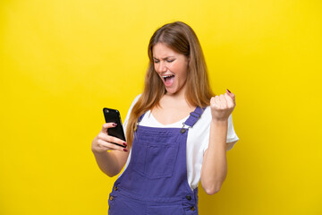 Young caucasian woman isolated on yellow background with phone in victory position