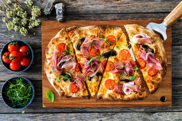 Pinsa Romana with prosciutto crudo , mozzarella and vegetables on wooden table
